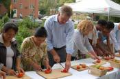 Chris Coleman at an outdoor table with others, cutting tomatoes. 