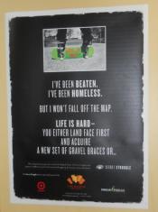 Photo of a black poster on a wall with a photo on it, of a side-turned skateboard, and the bottom of someones legs on it. Beneath that are the words "I've been beaten, I've been homeless, But I won't fall off the map. Life is hard - You either land face first and acquire a new set of gravel braces or..."  A Target store logo is on the bottom left of the poster. 