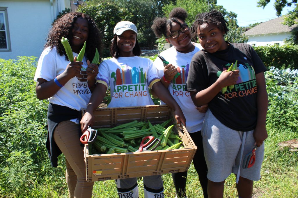 Aaliyah Demry and friends Nacory Holiday (left), Arieana Moore and Omariasha Houston celebrate the fruits of their work: a crate of newly picked okra grown in an AFC garden.